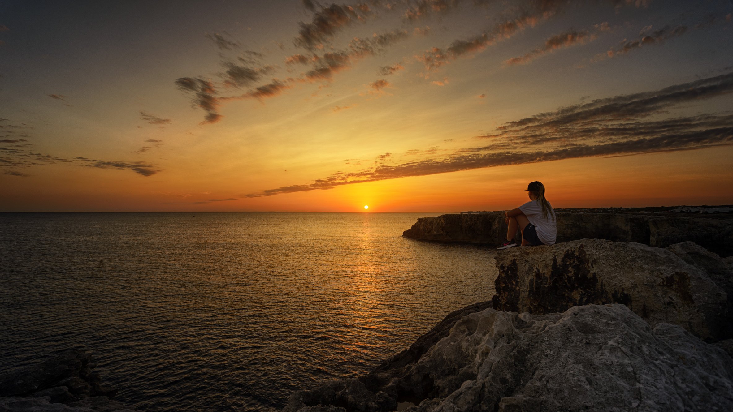 Photo of Person Sitting on Rock During Sunset